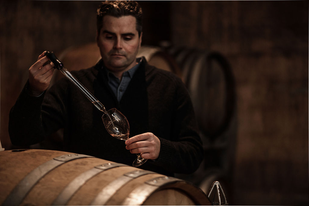 Wineamker using a glass tube to pour wine in a wine glass 